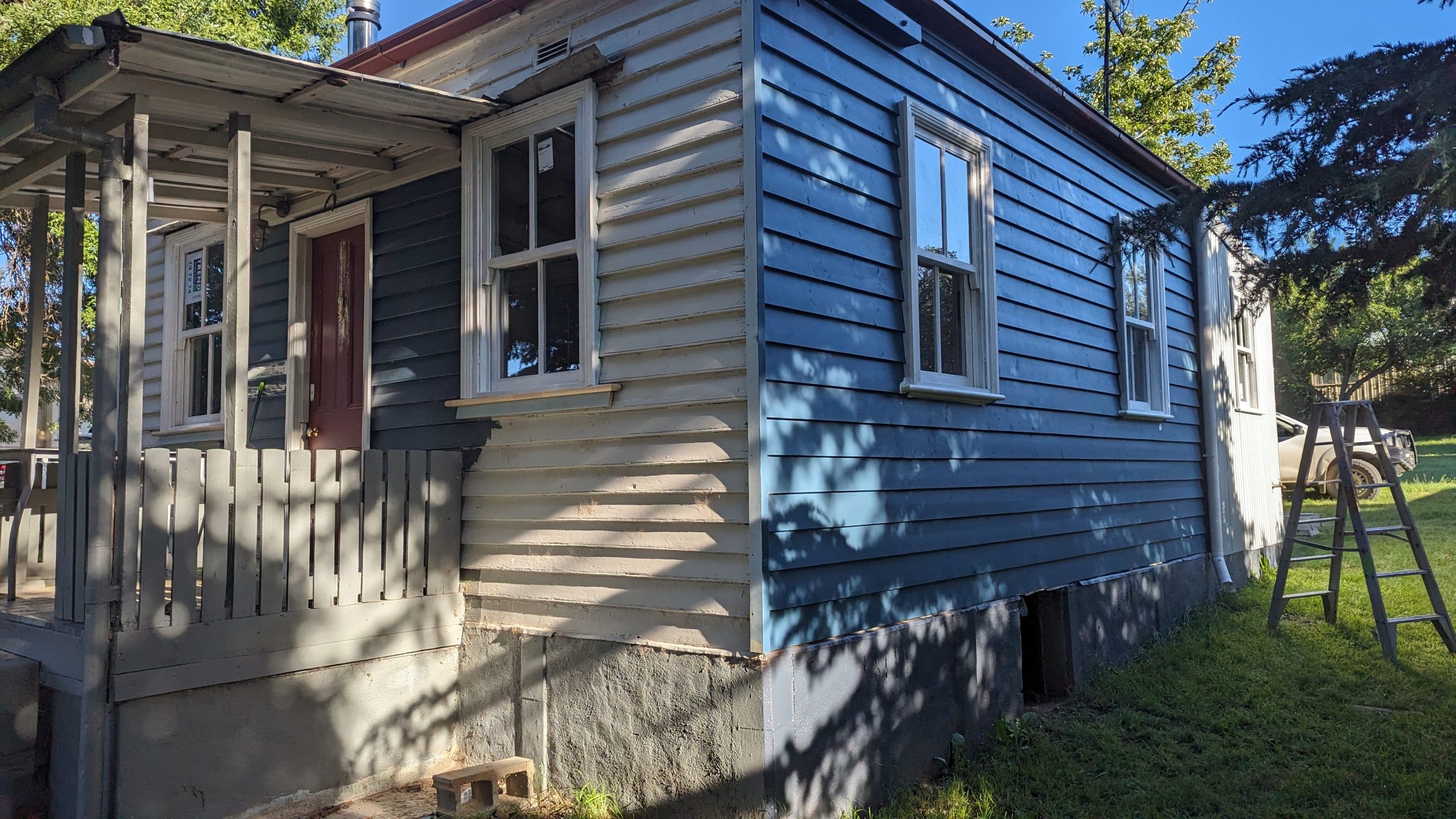 Weatherboard cottage under structural restoration with replacement boards spliced into the existing wall and the subfloor opened up below