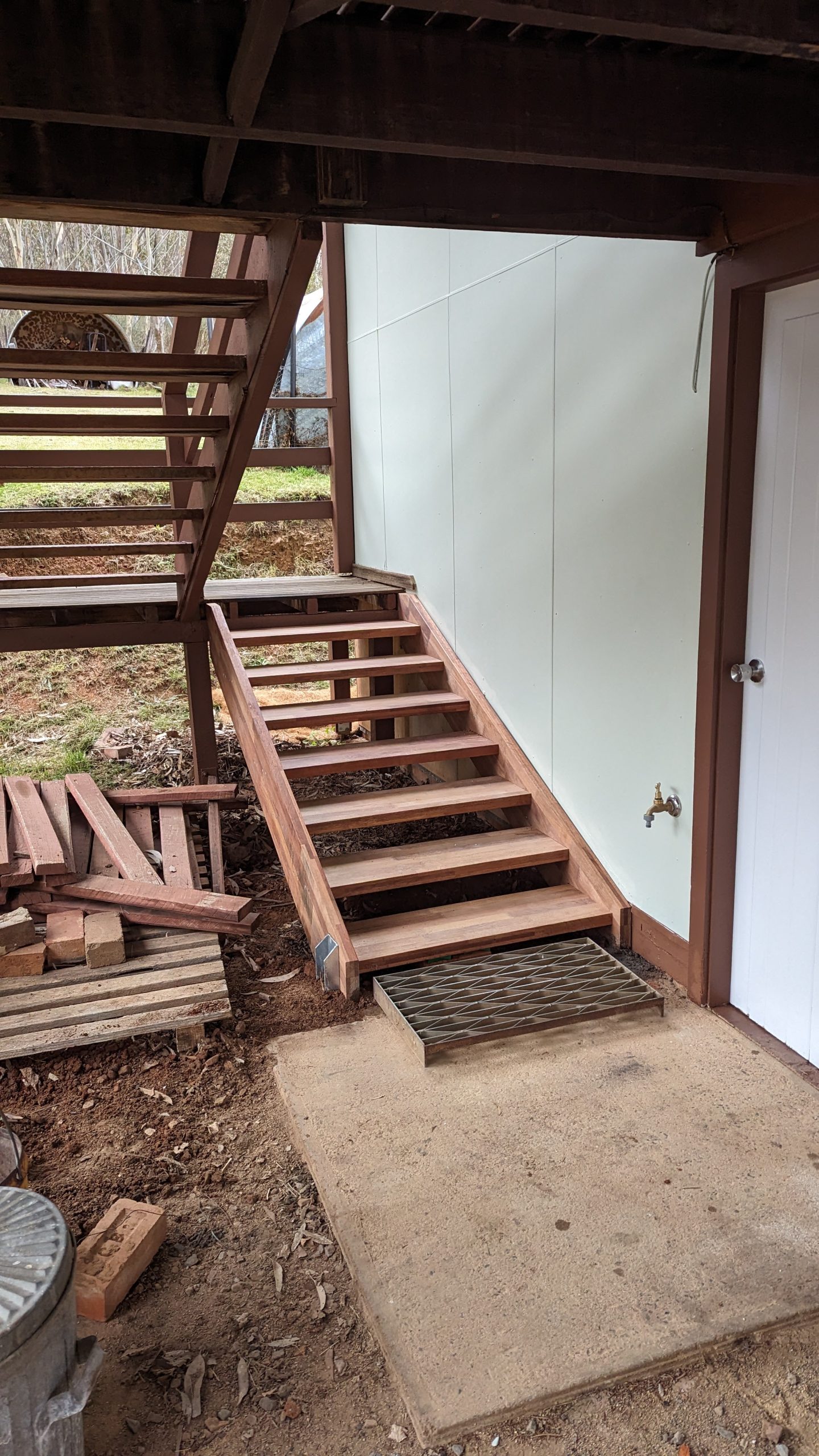 Replacement hardwood access stairs under an elevated deck, with the rotted original stair timbers stacked to one side